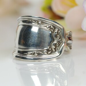 May include: A silver ring made from a repurposed spoon with an ornate design. The ring is wide and has a smooth, polished surface.