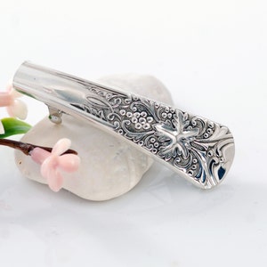 May include: Silver hair clip with an ornate design featuring a grapevine and leaves.