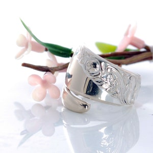 May include: A silver ring made from a vintage spoon, featuring an ornate floral design with roses and leaves. The ring is open and adjustable to fit different finger sizes.