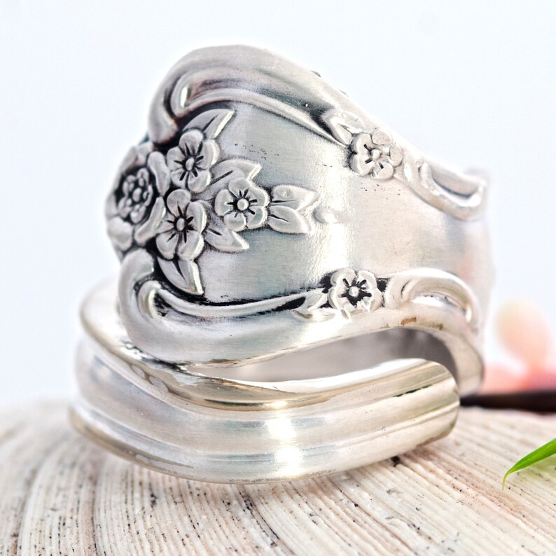 May include: A silver ring made from a vintage silverware spoon with a floral design. The ring is adjustable and can be worn on any finger.