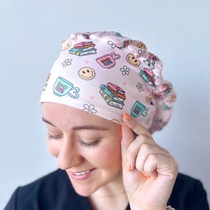 May include: Pink surgical scrub hat with a pattern of stacked books, coffee cups, and smiley faces. The text "Book Club" is printed on the coffee cups.