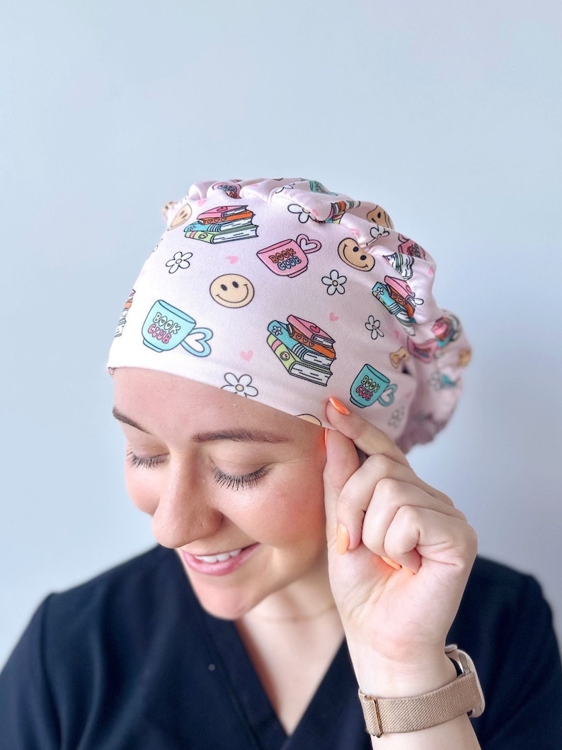 May include: Pink surgical scrub hat with a pattern of stacked books, coffee cups, and smiley faces. The text "Book Club" is printed on the coffee cups.