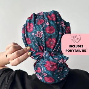 May include: A teal floral head wrap with a pink flower pattern, tied in a knot. The image includes a pink square with the text "INCLUDES PONYTAIL TIE" and a drawing of a ponytail tie.