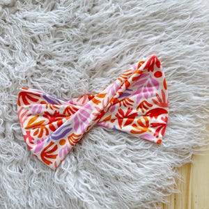 May include: A pink, orange, and purple patterned headband with a twisted design.