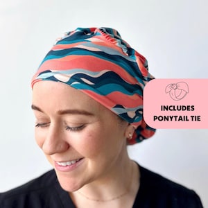 May include: A woman wearing a pink and blue patterned surgical scrub hat with a ponytail tie. The hat has a wavy pattern and is made of a soft, comfortable fabric.  Includes ponytail tie.