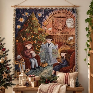 May include: A woven tapestry wall hanging featuring a holiday scene with three children in a room with a Christmas tree, a fireplace, and a Gryffindor crest. The text Gryffindor is visible above the fireplace. The tapestry has a fringed edge.
