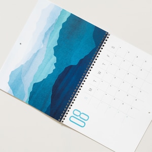 Wall calendar for 2024 with bright colorful abstract landscapes. Coil bound with pre-drilled hole for easy hanging. Calendar grid with space for notes. Opens up to 11x17 inches size. Month of August shown here.