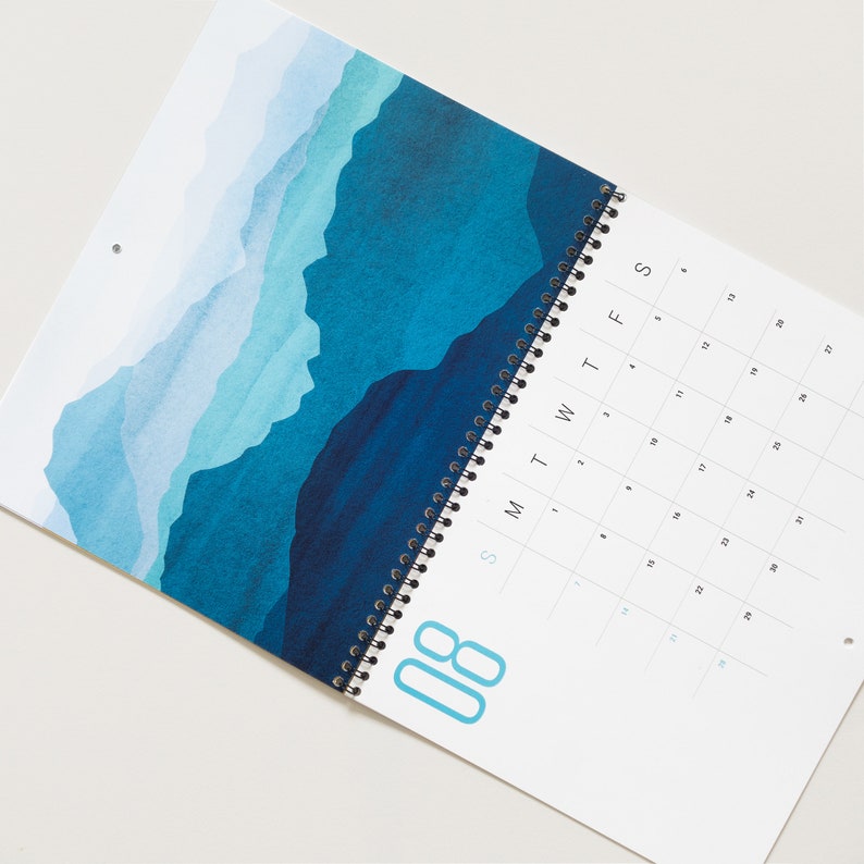 Wall calendar for 2024 with bright colorful abstract landscapes. Coil bound with pre-drilled hole for easy hanging. Calendar grid with space for notes. Opens up to 11x17 inches size. Month of August shown here.