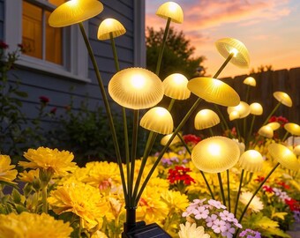 May include: A set of solar-powered garden lights shaped like mushrooms with glowing white caps on thin green stems. The lights are arranged in a cluster with a black solar panel base, positioned among yellow marigolds and small purple flowers.
