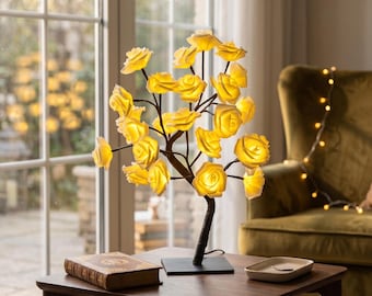 May include: A decorative tree lamp featuring multiple illuminated yellow rose-shaped blossoms attached to dark brown branches. The lamp has a square black base and emits a warm glow from each individual flower, creating a bright floral display.