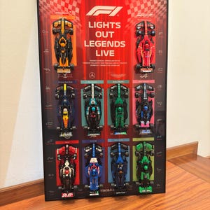 Pode incluir: Um quadro de parede com dez carros de corrida de Fórmula 1 em miniatura dispostos em grade. O texto central diz F1 LIGHTS OUT LEGENDS LIVE. Cada carro está montado acima do nome da sua equipa, incluindo McLaren, Ferrari, Red Bull e Mercedes.