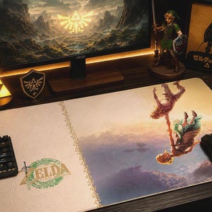 May include: A rectangular desk mat featuring a cream-colored section with the green The Legend of Zelda: Tears of the Kingdom logo and a larger section depicting two figures falling through a cloudy sky, with a black computer mouse resting on top.