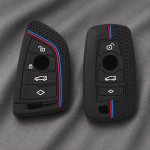 May include: Two black silicone key fob covers featuring a textured honeycomb pattern on one side and a vertical stripe in blue and red. Each cover displays white icons for locking, unlocking, boot release, and a diamond shape button.