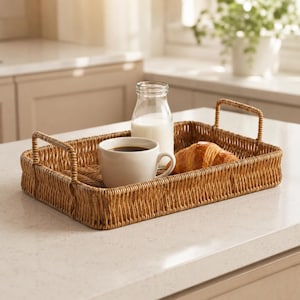 May include: A rectangular woven rattan tray with two side handles. Inside the tray sits a white ceramic mug filled with dark coffee, a clear glass bottle containing white milk, and a golden-brown flaky croissant resting on the woven base.