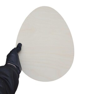 Könnte beinhalten: Ein flacher, eiförmiger Zuschnitt aus hellem, glattem Holz mit natürlicher Maserung. Das Objekt hat eine abgerundete Oberseite und eine etwas breitere Basis und bietet eine saubere, unbehandelte Oberfläche für verschiedene Bastelprojekte.