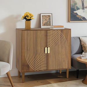 May include: A wooden cabinet with two doors featuring a white arched line pattern and two vertical gold handles. The cabinet stands on four tapered wooden legs and has a rectangular frame with a smooth brown wood grain finish throughout the exterior.