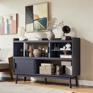 May include: A dark blue sideboard with a sliding fluted door, four tapered legs, and multiple open shelves. The unit is styled with various decorative items including a white bust, a ceramic vase, books, a small gramophone, and woven boxes.