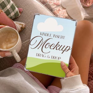 May include: A clear protective case for a Kindle device featuring a graphic insert with a light blue sky, a white cloud, and a green grassy hill. The text on the insert reads KINDLE INSERT Mockup DRAG & DROP in dark brown lettering.