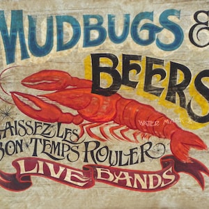 May include: A rustic sign with the words "MUDBUGS & BEERS" in blue and black lettering, and a large red crawfish illustration. The sign also includes the phrase "LAISSEZ LES BON TEMPS ROULER" and "LIVE BANDS" in a banner.