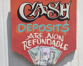 May include: A rectangular orange wooden sign with a scalloped bottom edge featuring the text CASH DEPOSITS ARE NON REFUNDABLE in black and teal lettering. Three prop twenty and fifty dollar bills are tucked into a slot at the bottom of the sign.