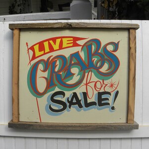 May include: A vintage wooden sign with a hand-painted message in bright colors. The sign reads "LIVE CRABS for SALE!" with a red, blue, and green color scheme.