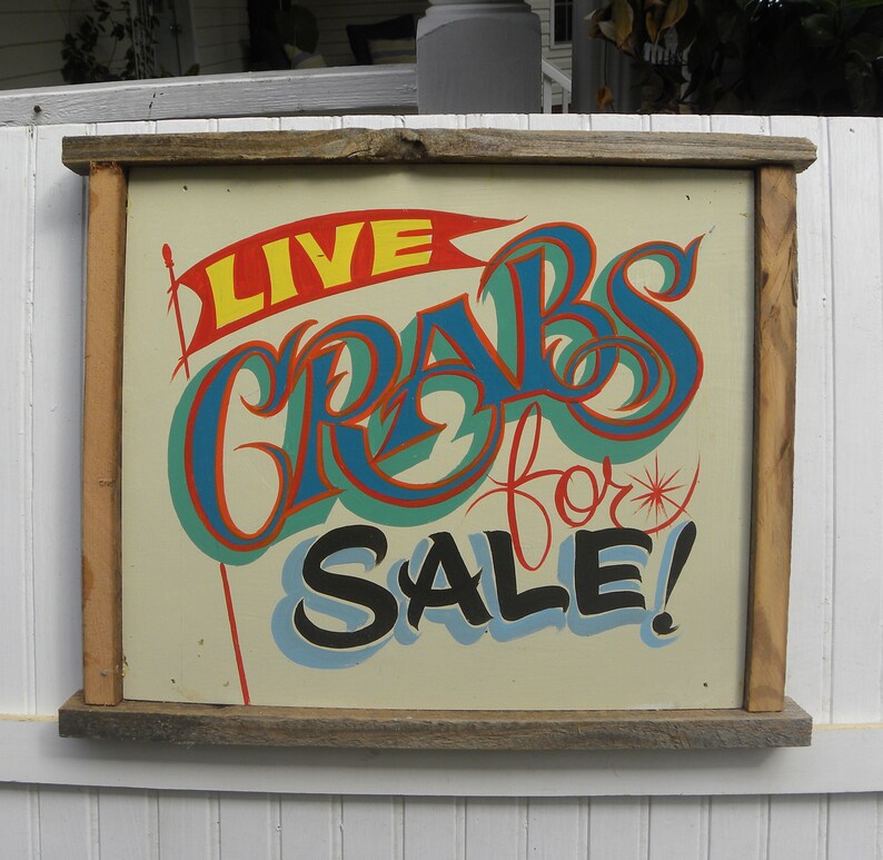 May include: A vintage wooden sign with a hand-painted message in bright colors. The sign reads "LIVE CRABS for SALE!" with a red, blue, and green color scheme.
