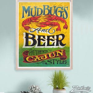 May include: A rectangular wall sign in a light wood frame featuring a yellow and green background. The text reads MUDBUGS And BEER AUTHENTIC CAJUN STYLE. Two red crawfish are illustrated in the center above the word BEER in black lettering.