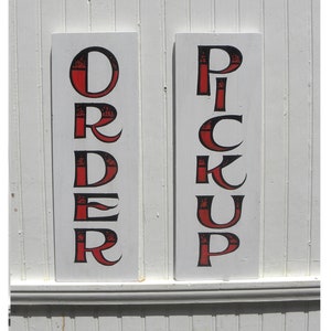 May include: Two white wooden signs with black lettering and red accents. The sign on the left says "ORDER" and the sign on the right says "PICK UP".