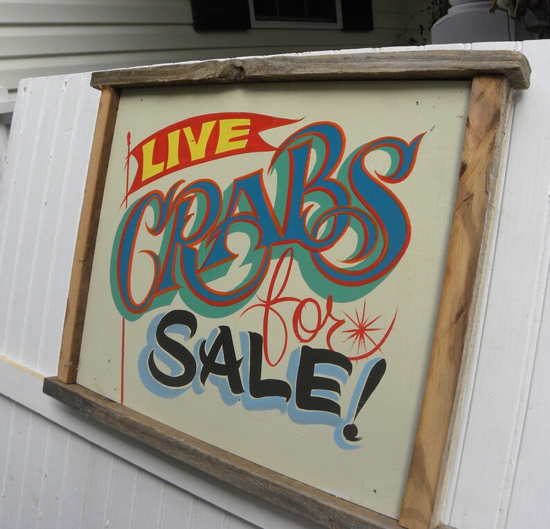 May include: A wooden sign with a hand-painted message that reads "LIVE CRABS for SALE!" in colorful lettering. The sign is framed in a rustic wooden frame.