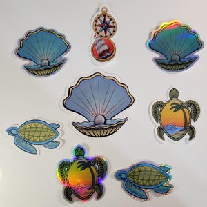 May include: Set of eight iridescent holographic stickers featuring a compass, seashells, and sea turtles. The stickers have a shiny, glittery finish and are perfect for adding a touch of whimsy to your belongings.