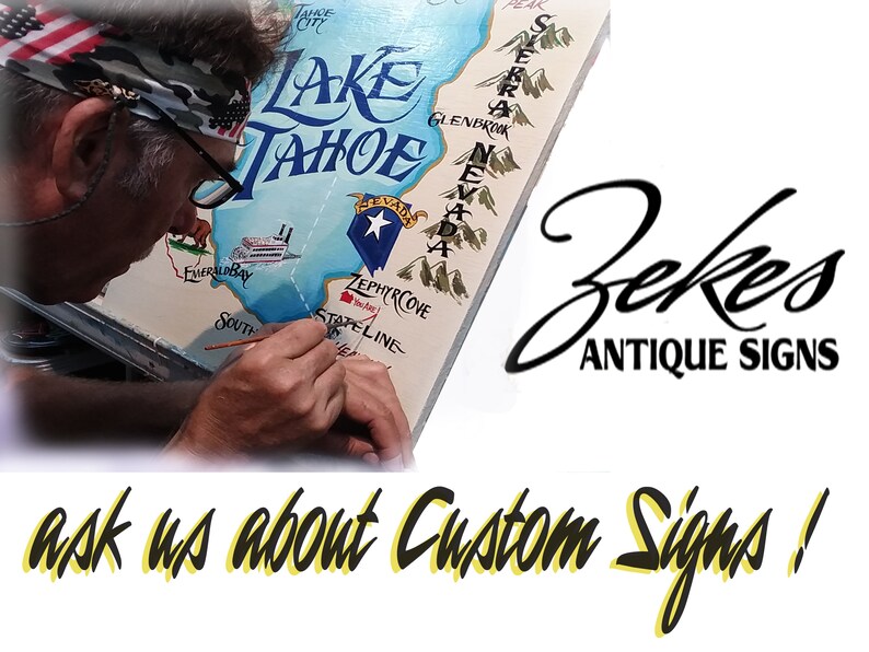 May include: A person paints a custom sign with a map of Lake Tahoe, California. The sign features the text "Lake Tahoe" and "Zekes Antique Signs". The text "ask us about Custom Signs!" is written in yellow and black.