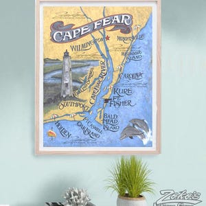 May include: A framed map print titled Cape Fear featuring a lighthouse, coastal towns, and dolphins. The map displays locations including Wilmington, Wrightsville, Masonboro Island, Carolina, Kure, Ft. Fisher, Bald Head Island, and Southport.