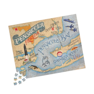 May include: A vintage-style jigsaw puzzle featuring a map of Pensacola, Florida, with landmarks and text. The puzzle includes illustrations of dolphins, airplanes, a lighthouse, and beach scenes. The puzzle is beige, blue, and tan.
