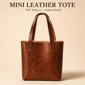 Op de afbeelding: Een bruine leren mini tote tas met twee verticale handvatten bevestigd met donkere metalen klinknagels. De tekst MINI LEATHER TOTE PDF Pattern + Video Guide staat in een donkerbruin lettertype boven de tas op een lichtbeige achtergrond.