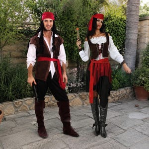 May include: Two pirate costumes consisting of white long-sleeved shirts, brown vests, black trousers, and red waist sashes. The outfits include red headscarves and dark brown or black knee-high boots. One costume features a brown lace-up bodice.