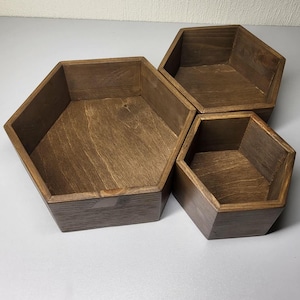May include: Three dark brown wooden boxes with a hexagonal shape. Each box features a smooth, stained finish that highlights the natural wood grain patterns on the interior base and the exterior vertical walls of the containers.
