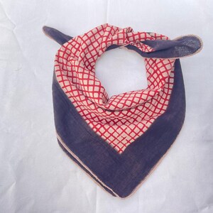 May include: A triangular bandana featuring a central red and white diamond grid pattern bordered by a solid dark navy blue fabric. The accessory is tied at the top, showcasing a folded design with visible stitched edges along the dark blue perimeter.