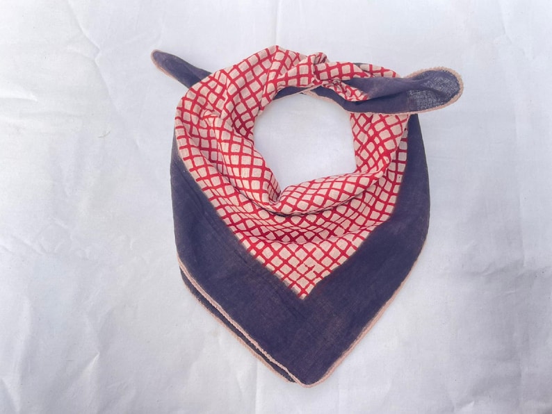 May include: A triangular bandana featuring a central red and white diamond grid pattern bordered by a solid dark navy blue fabric. The accessory is tied at the top, showcasing a folded design with visible stitched edges along the dark blue perimeter.