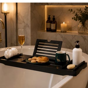 Könnte beinhalten: Ein schwarzes Badewannenablage mit verstellbarem Buch- oder Tablettständer, einem Stielglas mit bernsteinfarbener Flüssigkeit, einer grünen Tasse mit dem Wort Lucky, einem weißen Seifenspender, einem Stück Seife und einem Teller mit Keksen und Gebäck.