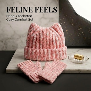 May include: A hand-crocheted set featuring a pink and white speckled beanie with cat-ear points and matching fingerless gloves. The text FELINE FEELS Hand-Crocheted Cozy Comfort Set is visible above the beanie, which has a ribbed texture.