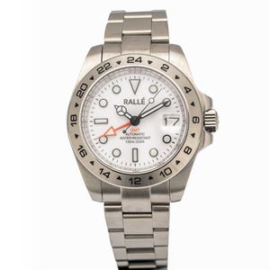 May include: A stainless steel wristwatch with a white dial, featuring a 24-hour bezel, luminous markers, and an orange GMT hand. The dial displays the text RALLÉ, GMT, AUTOMATIC, WATER RESISTANT, and 100m:330ft, with a date window at the three o'clock position.