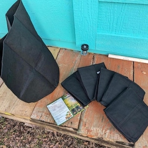 May include: A set of black fabric plant grow bags, including one upright open bag and several folded flat bags, accompanied by a small rectangular instruction card with printed text and a colorful garden illustration.