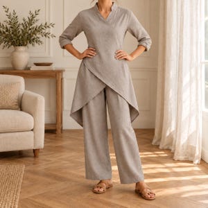 Puede incluir: Un conjunto de dos piezas de color gris claro que consta de una túnica de manga larga con escote en V y un dobladillo asimétrico estilo cruzado que cae por debajo de las caderas, combinado con pantalones anchos a juego. Tela de color sólido.