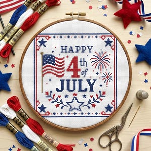May include: A circular wooden embroidery hoop containing a cross-stitch design with the text "HAPPY 4th of JULY". The design features a small American flag, fireworks, and star motifs in red, white, and blue thread on a white fabric background.