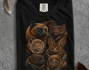 May include: A black t-shirt featuring a detailed graphic print of six different bats in shades of brown and tan. The shirt has a Comfort Colors brand label at the inner neckline. The design displays various bat species with distinct facial features.