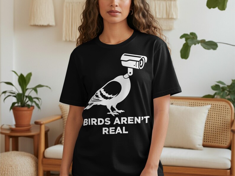 Black t-shirt with white graphic of a bird with a security camera for a head, text reads "BIRDS AREN'T REAL".