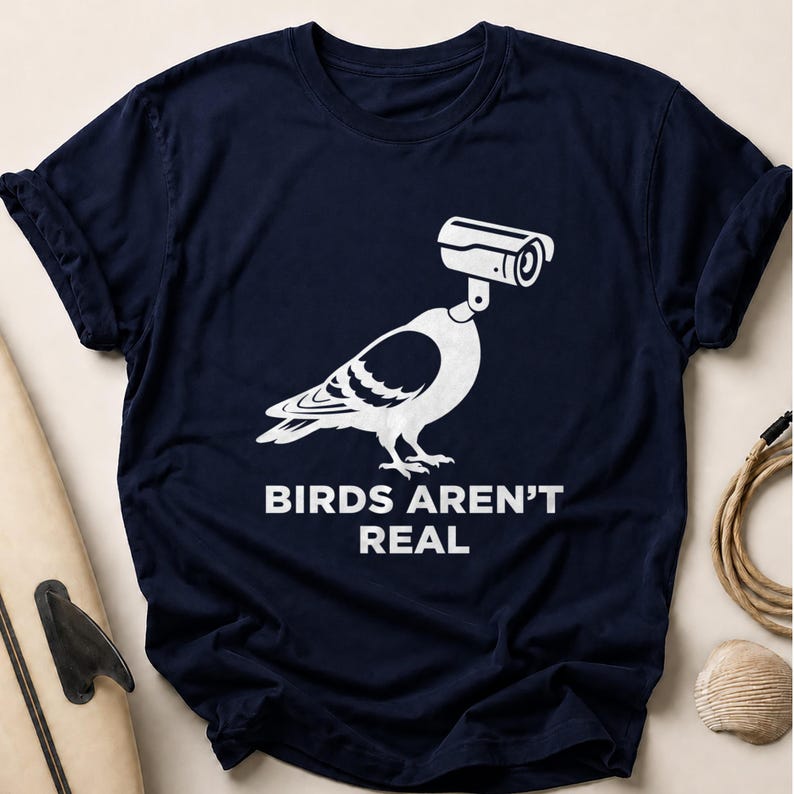 Navy t-shirt with a graphic of a pigeon wearing a surveillance camera for a head, text reads "BIRDS AREN'T REAL".