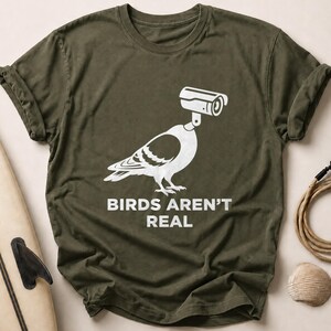 Olive green t-shirt with "BIRDS AREN'T REAL" text and a pigeon with a camera.