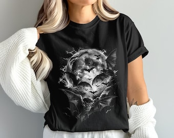 May include: A black short-sleeved t-shirt featuring a detailed graphic print of a large, bright full moon surrounded by numerous flying bats in various sizes. The artwork is rendered in shades of white, gray, and black, creating a high-contrast scene.