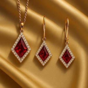 May include: A jewelry set consisting of a necklace and two matching drop earrings. Each piece features a kite-shaped deep red gemstone framed by a border of small white stones, all set in a gold-toned metal. The necklace includes a gold chain.